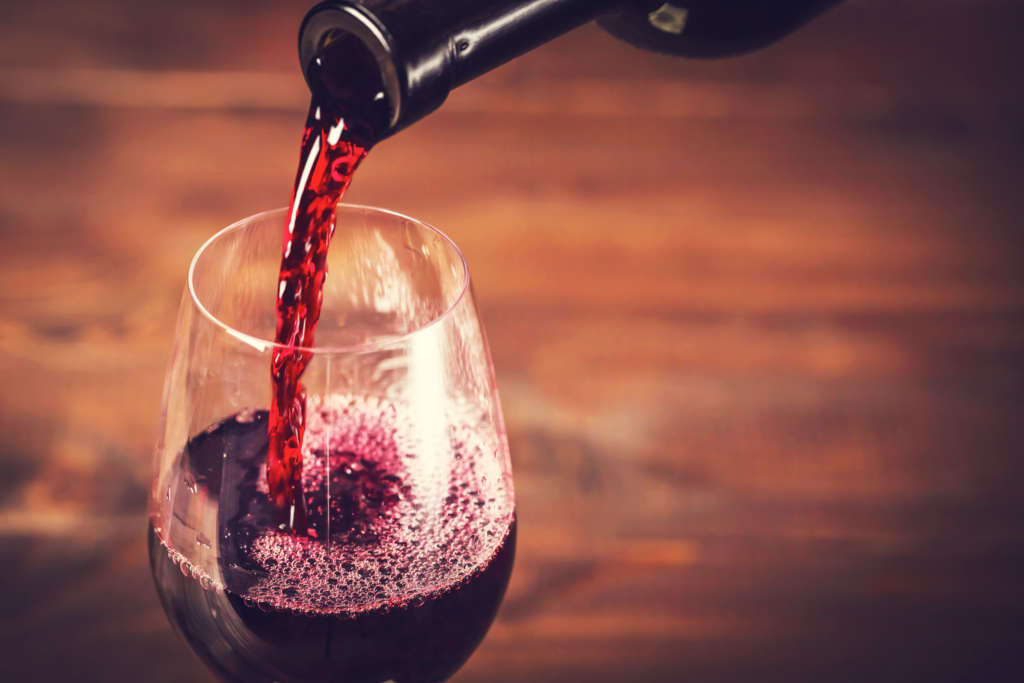 51975832 - pouring red wine into the glass against wooden background